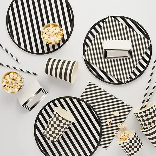 Monochrome party tableware with black and white striped plates, cups, napkins, and popcorn containers arranged on a light background